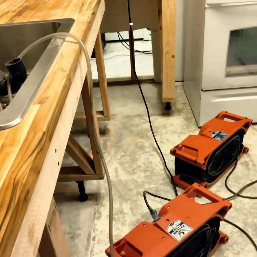 Orange air movers on a stained floor beside kitchen counters during a Commerce City dry-out