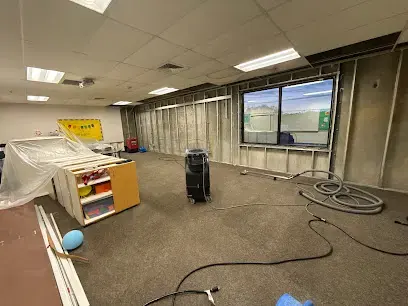 Dehumidifier and cords running in an emptied commercial room during water damage drying
