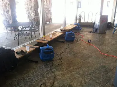 Air movers spread across a wet floor with furniture moved aside during structural drying