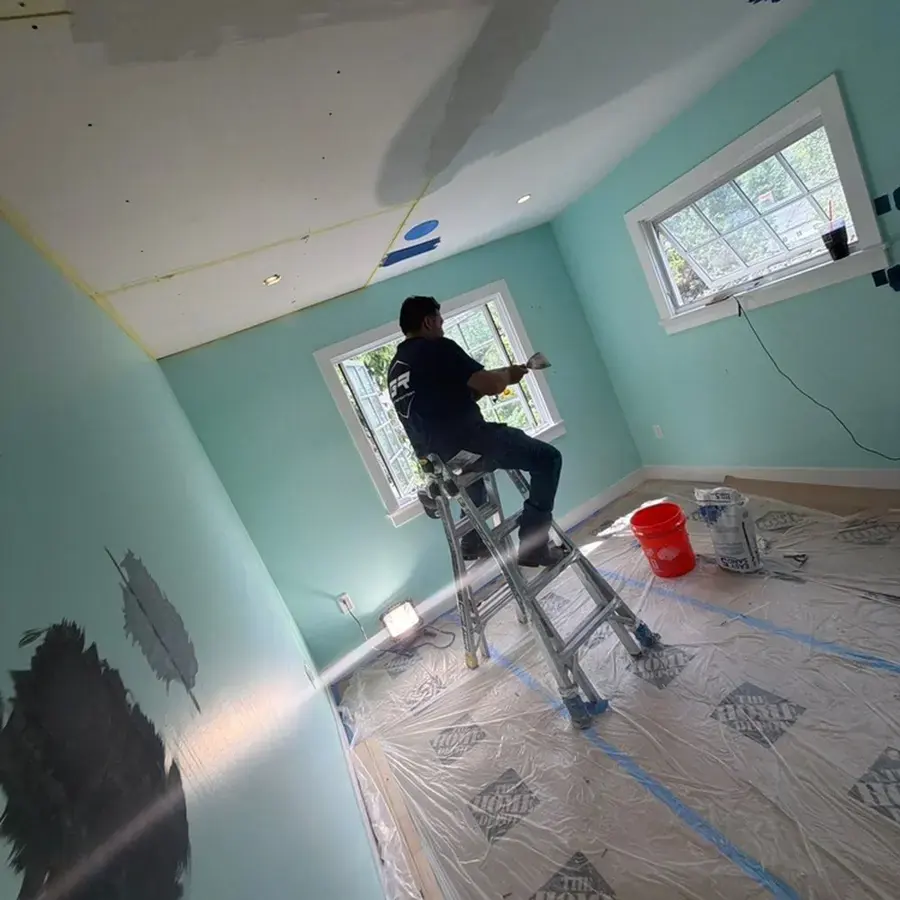 Worker on a ladder with plastic sheeting laid over the floor during a water damage dry-out