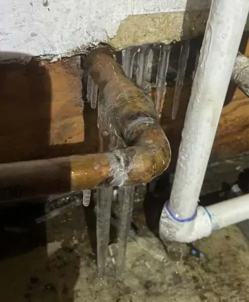 Copper and plastic pipes coated in ice in a cold basement ceiling